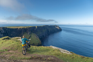 Woman on Cliff of Moher. Female cyclist admires spectacular landscape, tranquility, relaxation.