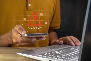 Man working on laptop and receive Scam Alert Warning notification pr fraud message on his smartphone