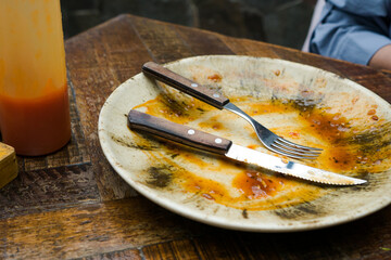 A cream-colored plate with a beautiful pattern shows leftover food, including a knife and fork. Some sauce remains on the plate, indicating the end of a meal