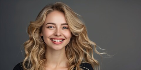 Naklejka premium A young woman with blonde wavy hair exudes charm, confidence, and happiness in a studio portrait. She radiates an attractive and carefree aura, embodying modern elegance and youthful joy