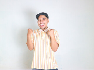 young asian man wearing striped polo shirt celebrating victory and rejoicing because he has achieved success while shouting and raising his hands