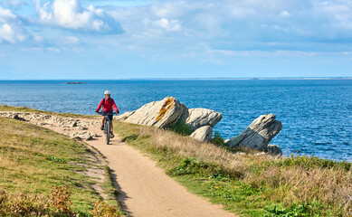 active senior woman cycling with her electric mountain bike at the wild coast of Quiberon peninsula, Brittany, France