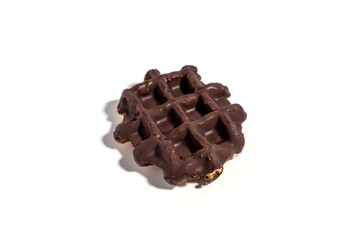 A chocolate waffle sits on a white background. The waffle is covered in chocolate and has a square shape Sweet pastries isolated on white background.