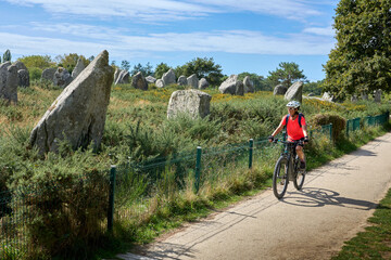 Woman cycling along the megalithic alignments of Carnac in Brittany, France