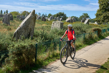Woman cycling along the megalithic alignments of Carnac in Brittany, France