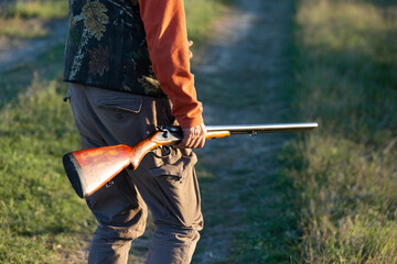 Mature hunter man holding a shotgun and walking through a field
