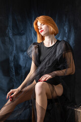 A young red-haired girl in a black bodysuit poses in the studio against a dark background.