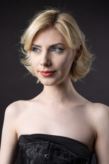 Naklejka premium Expressive young blonde under a bob in the studio. In a black corset and dress.