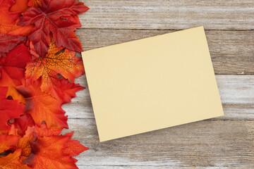 Obraz premium Fall leaves with a blank greeting card on rustic wood