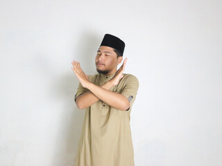 Asian Muslim man wearing a peci shows crossed arms, x sign gesture, gesturing warning or...