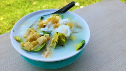 Es teler in a white bowl with a garden background is a popular Indonesian drink filled with several fruits such as avocado, young coconut and jackfruit, then mixed with sweetened condensed milk