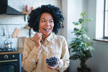 Photo of young smiling healthy laughing african woman in casual eating breakfast and fruits berries...