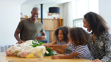 Family Returning Home From Shopping Trip Unpacking Plastic Free Grocery Bags On Table