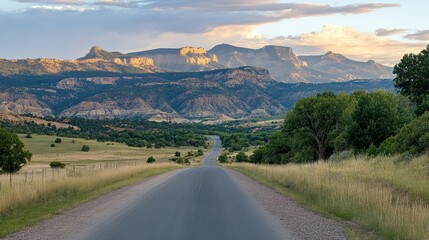 Scenic Road Leading Through Green Fields with Majestic Mountains in the Background at Sunset, Capturing the Beauty of Nature and Open Landscapes
