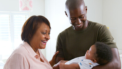Fototapeta premium Proud Grandmother With Adult Son Cuddling Baby Grandson In Nursery At Home