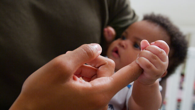Close Up Of Baby Son Gripping Father's Finger As He Cuddles Him In Nursery At Home