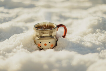 Steaming cup of hot tea on a snow-covered surface at sunrise. Concept of winter coziness, warmth,...