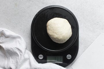 Overhead view of challah dough on a black kitchen scale, top view of homemade challah bread dough being weighed on a scale, process of making challah