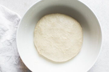 Overhead view of proofed challah dough in a white mixing bowl, top view of homemade challah dough rising in a white mixing bowl, process of making challah