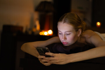 woman using smartphone during relaxing massage in wellness center. Thai Massage and spa therapy. Beautiful caucasian Woman Getting service aromatherapy massage Spa Treatment