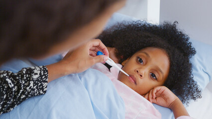 Mother Caring For Sick Daughter Ill In Bed At Home Taking Temperature With Thermometer