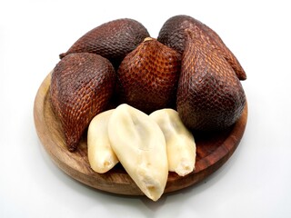 A close-up of fresh salak fruit or snake fruit on a wooden plate and isolated on a white background