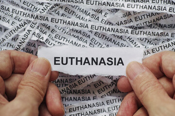 A man holding a piece of paper with the word Euthanasia typed on it in his hands over crumpled strips of newspaper. Close up.