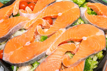 Raw fresh cut salmon fish steak slices on tomatoes,champignons mushrooms,broccoli vegetables, organic sea bass preparing for cooking,baking in stove.healthy diet food