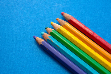 close up of colored wooden pencils in a row, on blue background. top view