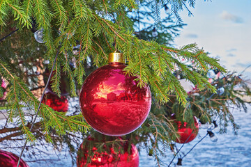 Close up of red Christmas ball ornament reflecting sunset, hanging on green tree branch