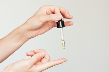A woman applying a moisturizing serum from a pipette to her index finger for application to the...