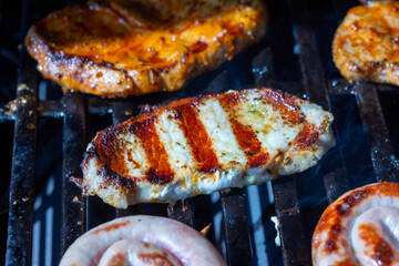 Marinated pork steak and chicken steak on the grill grate with flames