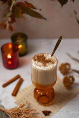Autumnal spiced pumpkin latte with whipped cream, cinnamon and maple sirup with leaves and candles on background. Halloween or Thanksgiving drink for single serving. Coffee as a dessert