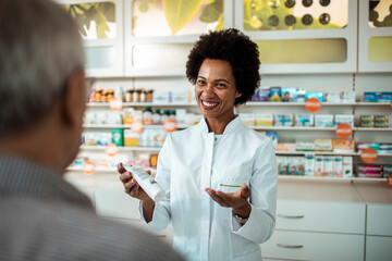 Female pharmacist showing medication bottle to senior male customer at pharmacy drugstore