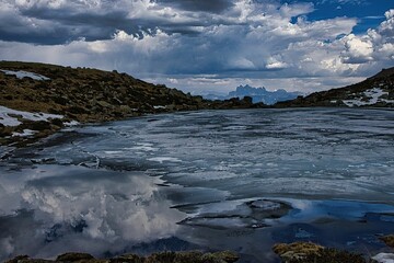 Serene frozen lake with dramatic clouds and peaks.