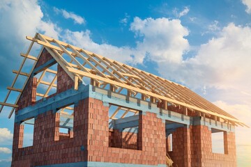 unfinished house under construction. The house features exposed red brick walls and a wooden roof framework.