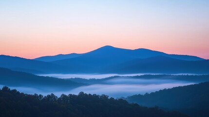 Obraz premium A serene mountain landscape at dawn, featuring layered hills shrouded in mist under a soft pastel sky.