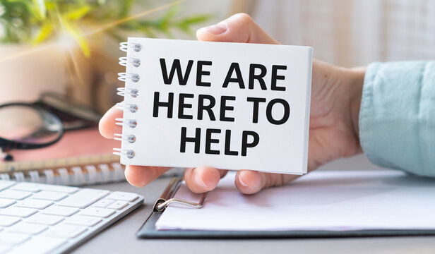 Closeup on business woman holding a card with We are here to Help message, business concept image with soft focus background