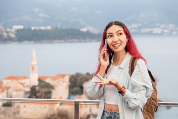 A female tourist with a backpack and phone stands against the backdrop of Budva, Montenegro, highlighting the concept of travel connection SIM cards, roaming rates, and internet costs.