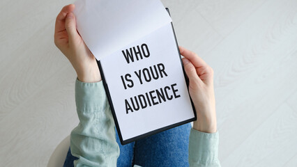 Who is Your Audience text on blank business card being held by a woman's hand with blurred...