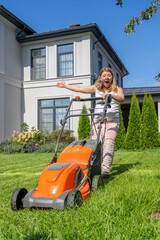 A woman joyfully operates a lawn mower, showcasing her yard maintenance skills in a well-kept garden under clear blue skies