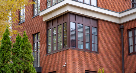 A contemporary brick building features expansive windows, nestled among lush greenery in a peaceful residential area during daylight