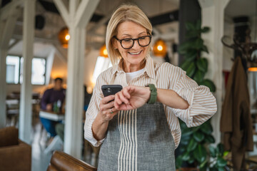 mature woman waitress stand at restaurant and use cellphone check time