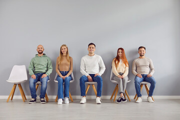 Naklejka premium Group portrait of young happy people chair sitting in easy pose, one vacant place. Diverse, together as team, friends gathered showing liking, affection and support, fellows in good relationships