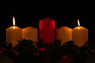 four white advent candles in a row where two are lit, with a red unlit Christ candle in the center,...