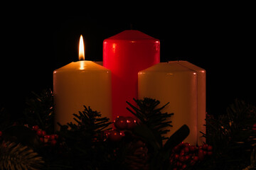 four white advent candles, one of them lit, with an unlit red christ candle in the center.