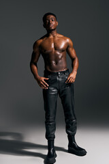 A young, handsome African American man poses confidently without a shirt, showcasing toned muscles and stylish black pants.