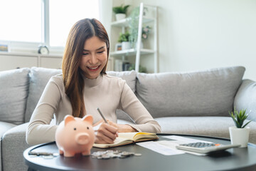 Young woman saving money monthly expenses putting coin in to piggy bank on the table.