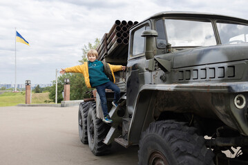 boy stands on step of military armored vehicle, multiple launch rocket system. Russian invasion of Ukrainian territory. Pride of Armed Forces of Ukraine. Stop war. Exhibition of military equipment