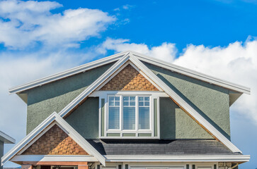 Top of grey stucco luxury house with shingle roof, red and yellow trees and nice windows in Summer in Vancouver, Canada, North America. Day time on June 2024.